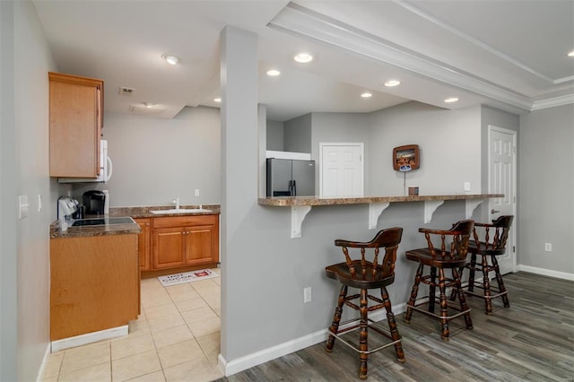 kitchen with sink, stainless steel fridge, stone countertops, a kitchen bar, and range