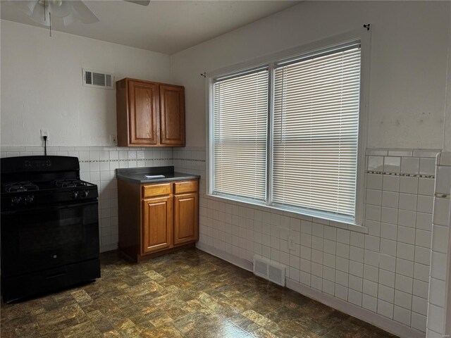 kitchen featuring black gas stove, a healthy amount of sunlight, and tile walls