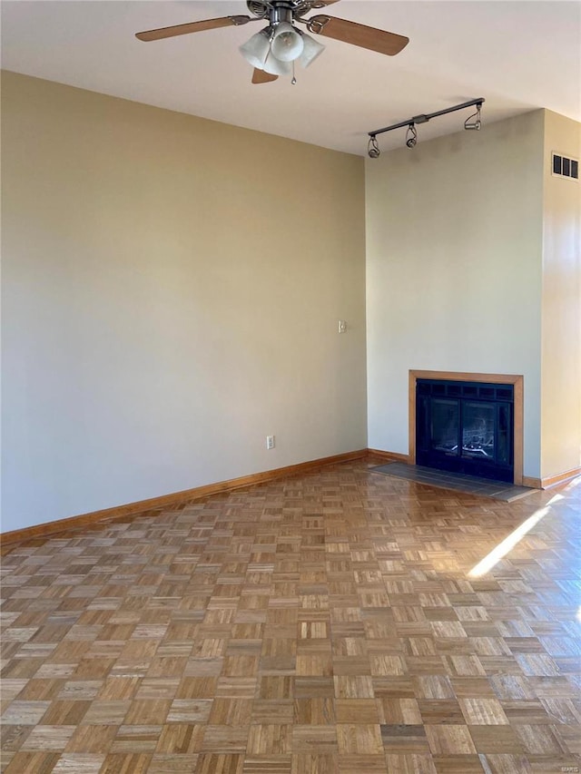 unfurnished living room with visible vents, rail lighting, a fireplace, baseboards, and ceiling fan