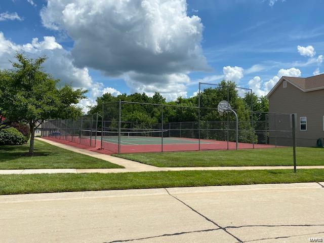 view of tennis court featuring basketball hoop and a lawn