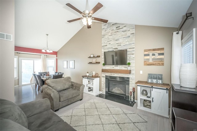 living room with high vaulted ceiling, ceiling fan with notable chandelier, light hardwood / wood-style flooring, and a tile fireplace