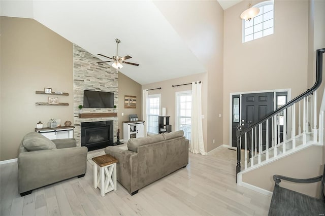 living room with a tiled fireplace, ceiling fan, high vaulted ceiling, and light hardwood / wood-style floors