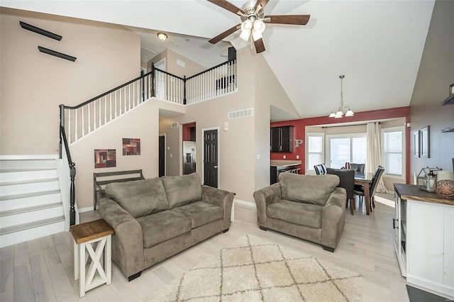 living room featuring a towering ceiling, ceiling fan with notable chandelier, and light wood-type flooring