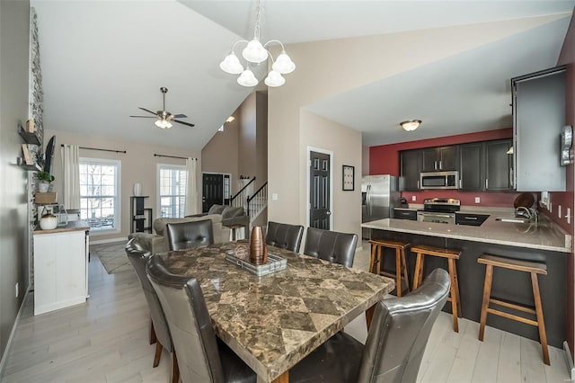 dining space featuring ceiling fan with notable chandelier, lofted ceiling, light hardwood / wood-style floors, and sink