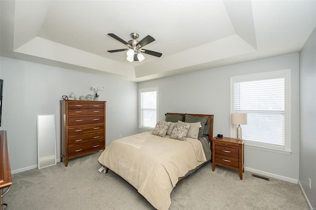 bedroom with light carpet, a tray ceiling, and ceiling fan