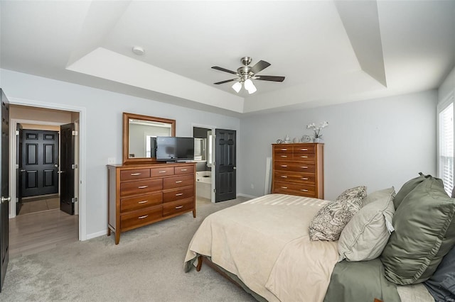 bedroom with light carpet, connected bathroom, a tray ceiling, and ceiling fan