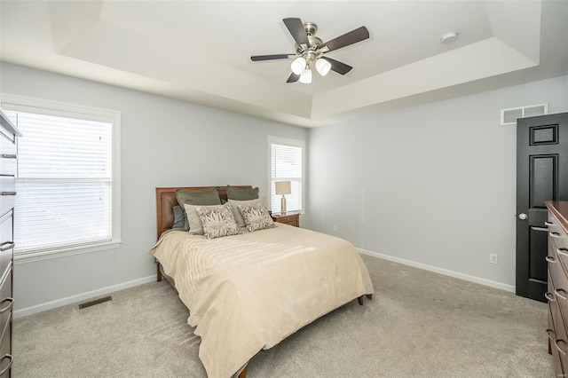 bedroom featuring light carpet, ceiling fan, and a tray ceiling