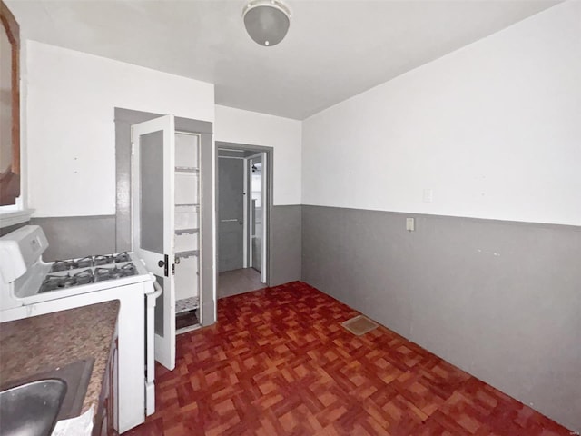 kitchen with dark parquet flooring, white gas stove, and sink