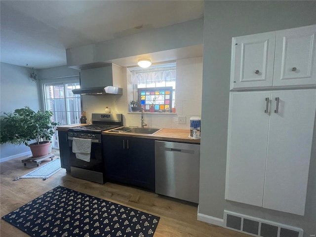 kitchen with exhaust hood, sink, white cabinetry, light wood-type flooring, and appliances with stainless steel finishes