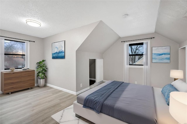 bedroom featuring lofted ceiling, a textured ceiling, and light wood-type flooring