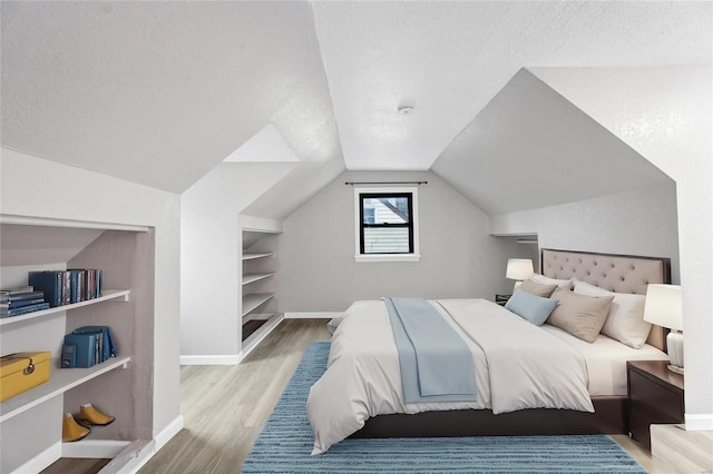 bedroom with lofted ceiling, light wood-type flooring, and a textured ceiling