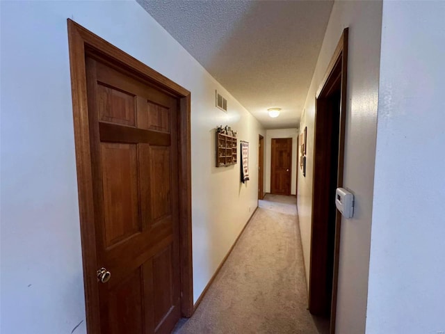 corridor with light colored carpet and a textured ceiling