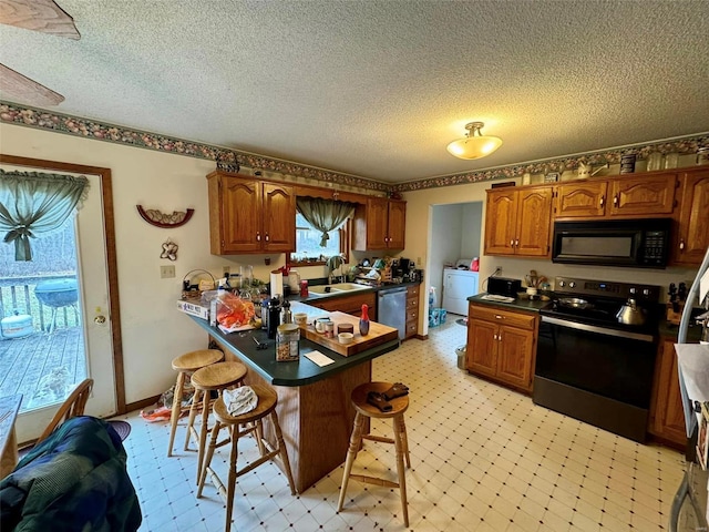 kitchen featuring sink, kitchen peninsula, a textured ceiling, a kitchen bar, and appliances with stainless steel finishes