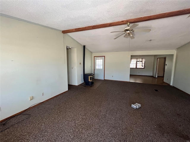 carpeted spare room with a textured ceiling, ceiling fan, lofted ceiling with beams, and a wood stove