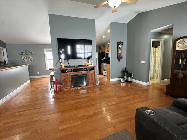 living room with a fireplace, ceiling fan, hardwood / wood-style floors, and vaulted ceiling