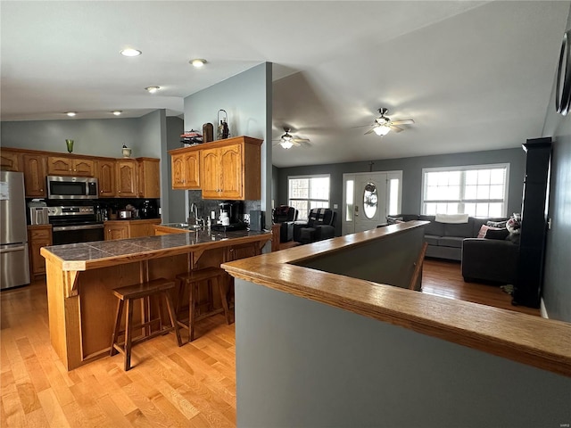 kitchen featuring backsplash, kitchen peninsula, vaulted ceiling, a breakfast bar, and appliances with stainless steel finishes