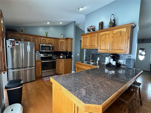 kitchen featuring backsplash, sink, vaulted ceiling, kitchen peninsula, and stainless steel appliances