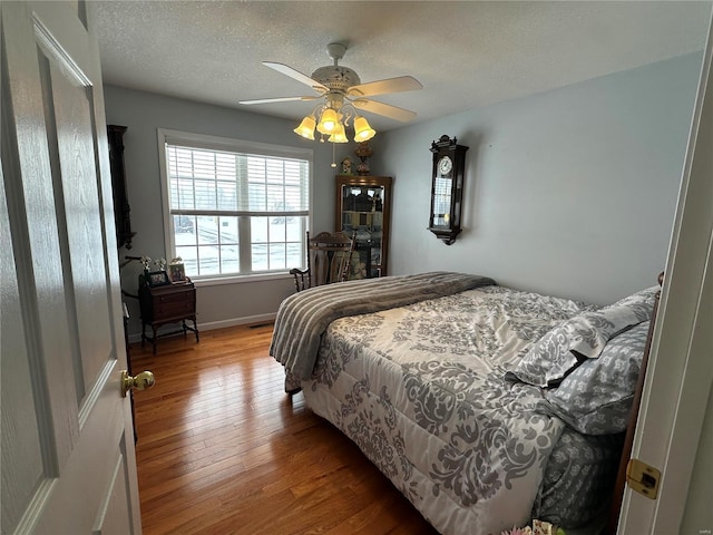 bedroom with ceiling fan, wood-type flooring, and a textured ceiling