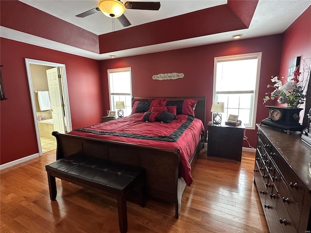 bedroom featuring hardwood / wood-style floors, connected bathroom, a tray ceiling, and ceiling fan