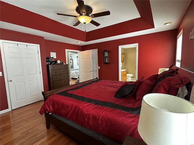 bedroom with hardwood / wood-style floors, connected bathroom, a raised ceiling, and ceiling fan