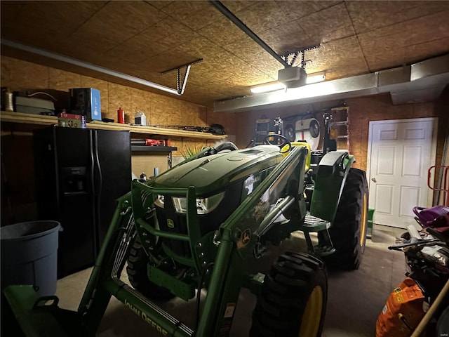 garage featuring a garage door opener, black refrigerator with ice dispenser, and wood walls