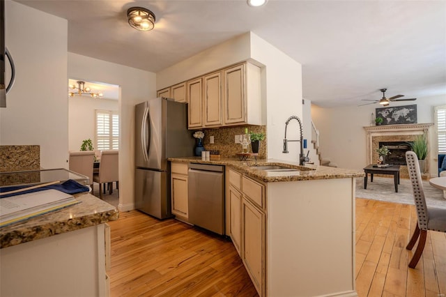 kitchen with sink, light stone counters, kitchen peninsula, cream cabinets, and appliances with stainless steel finishes