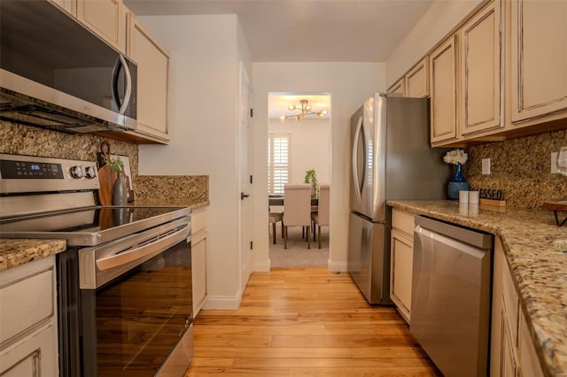 kitchen featuring an inviting chandelier, light stone counters, backsplash, light hardwood / wood-style floors, and appliances with stainless steel finishes