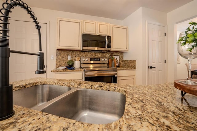 kitchen featuring tasteful backsplash, light stone counters, cream cabinets, and stainless steel appliances