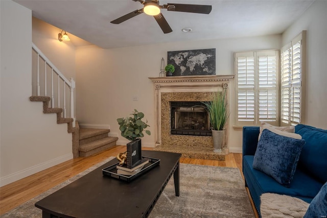 living room with a premium fireplace, ceiling fan, and wood-type flooring