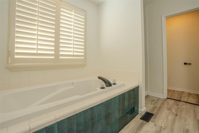 bathroom featuring wood-type flooring and tiled tub