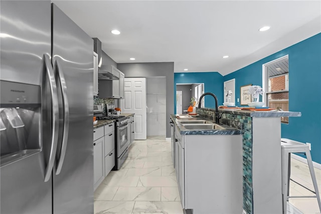 kitchen with gray cabinets, appliances with stainless steel finishes, backsplash, wall chimney range hood, and sink