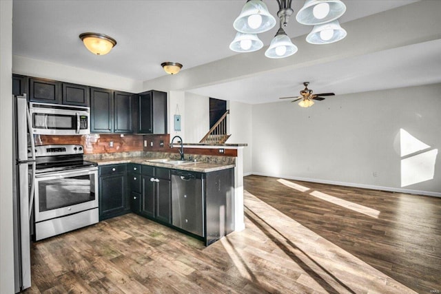 kitchen with a peninsula, dark wood-style flooring, a sink, appliances with stainless steel finishes, and ceiling fan with notable chandelier