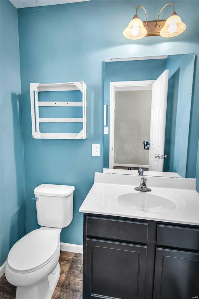 half bath with toilet, vanity, baseboards, and wood finished floors