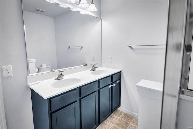 bathroom with double vanity, visible vents, toilet, and a sink