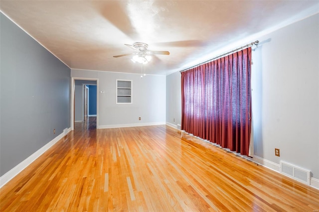 empty room featuring ceiling fan, built in shelves, and hardwood / wood-style flooring