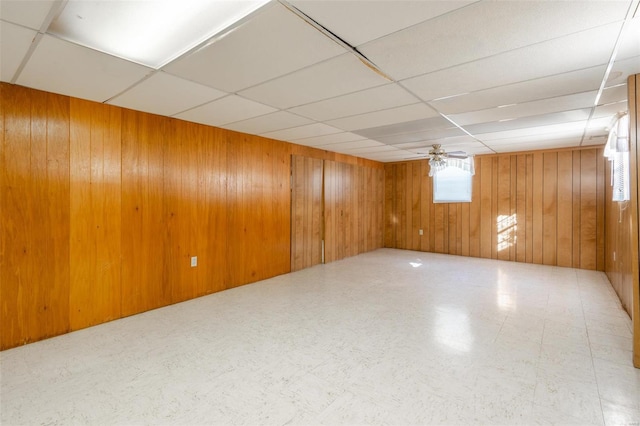 basement with a paneled ceiling, wooden walls, and ceiling fan