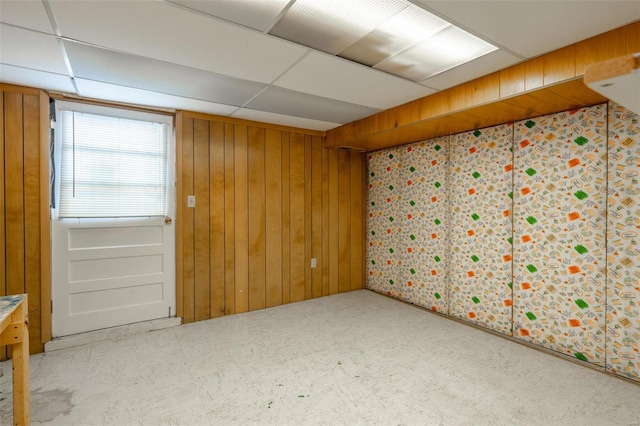 unfurnished room with a drop ceiling and wooden walls