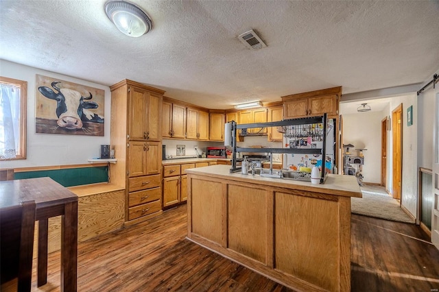 kitchen featuring dark hardwood / wood-style flooring, a center island with sink, and a textured ceiling