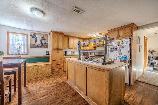 kitchen with dark wood-type flooring, an island with sink, white fridge, and a textured ceiling