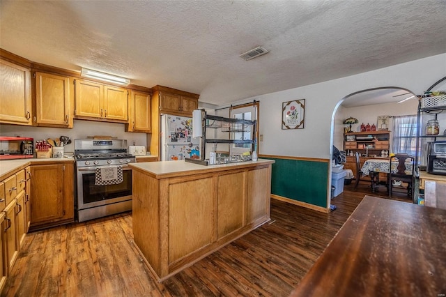 kitchen featuring dark wood-type flooring, gas stove, a textured ceiling, a kitchen island, and white fridge