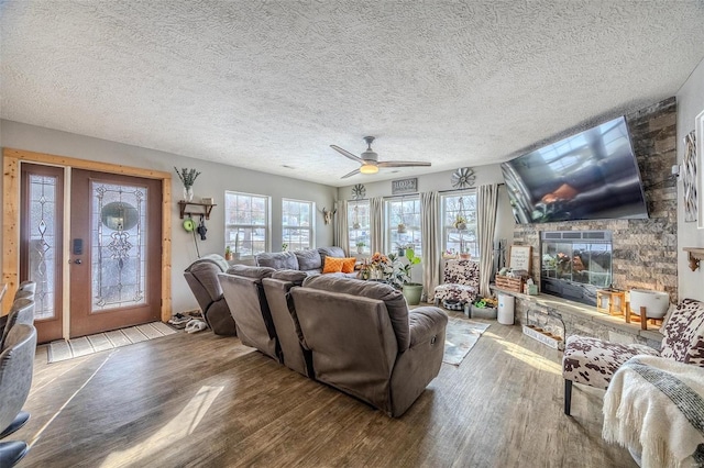 living room with ceiling fan, light wood-type flooring, a textured ceiling, and a fireplace