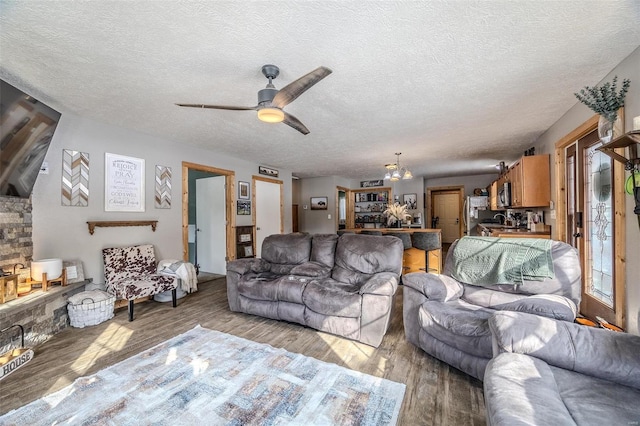 living room with a textured ceiling, light wood-type flooring, and ceiling fan with notable chandelier