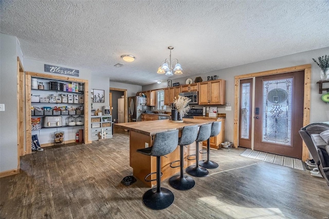 kitchen with wood-type flooring, a kitchen bar, hanging light fixtures, and appliances with stainless steel finishes