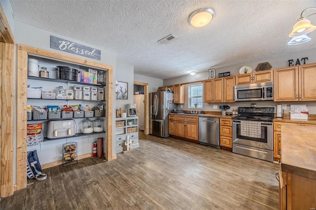 kitchen with wooden counters, appliances with stainless steel finishes, a textured ceiling, dark hardwood / wood-style floors, and sink