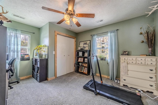 exercise area featuring a textured ceiling, ceiling fan, and light colored carpet