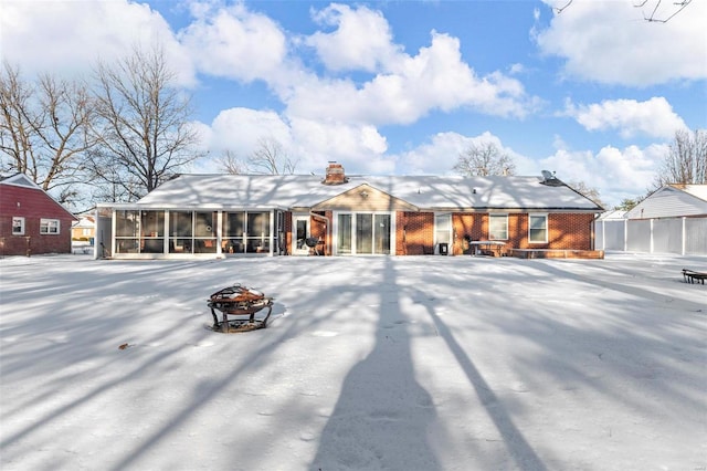 snow covered house with an outdoor fire pit and a sunroom