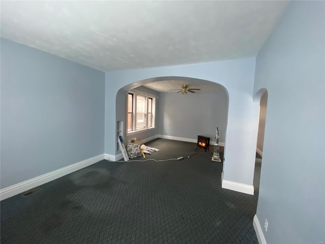 spare room with dark colored carpet, ceiling fan, and a wood stove