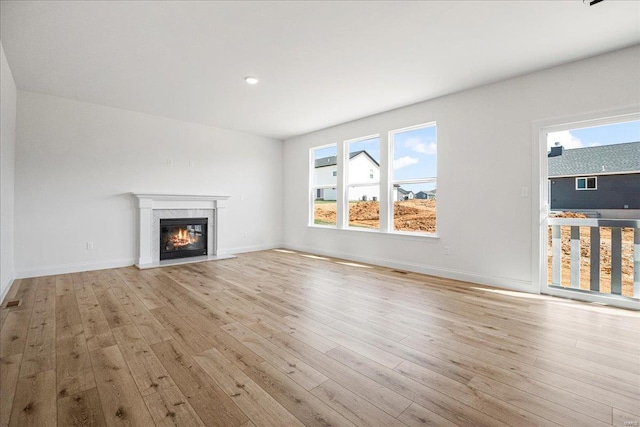 unfurnished living room featuring a wealth of natural light, a glass covered fireplace, and wood finished floors