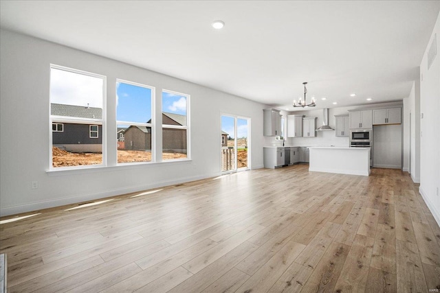 unfurnished living room featuring light wood-type flooring, an inviting chandelier, baseboards, and recessed lighting