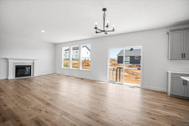 unfurnished living room with light wood-type flooring, baseboards, a chandelier, visible vents, and a high end fireplace